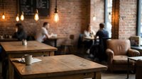Cozy coffee shop interior with wooden tables, exposed brick walls, pendant lighting and blurred customers creating warm atmospheric dining space.