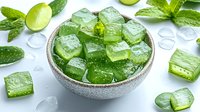 Green aloe vera jelly cubes in ceramic bowl with fresh mint leaves and water drops on white background, refreshing natural skincare ingredient.