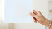 Close-up of a hand holding a blank white card or paper against a neutral beige background, suitable for mockups and presentations.