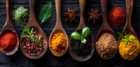 Vibrant aromatic spices and herbs in wooden spoons on dark background, colorful seasoning mix including turmeric, paprika, star anise and peppercorns for cooking.