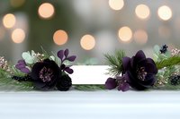 Dark purple hellebore flowers and winter greenery frame blank card on white surface with soft bokeh lights background, creating romantic holiday mood.