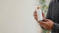 Mature man with medium skin tone holding white cosmetic bottle with wooden cap for skincare, lotion, or personal care product packaging mockup.