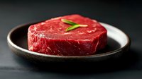 Fresh raw beef tenderloin steak garnished with rosemary on rustic ceramic plate against dark background, close up view of marbled meat texture.