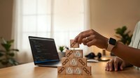 African American businessman building wooden blocks with dollar symbols at modern office desk with laptop displaying financial data for investment planning.