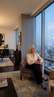 Mature blonde businesswoman relaxing in luxury high-rise apartment with city skyline view at dusk, modern interior design for lifestyle and success concepts.
