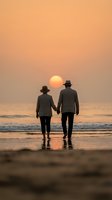 Senior couple walking hand in hand on a beach at sunset, golden sky reflecting on wet sand, waves in background.