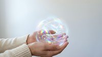 Close-up of hands holding iridescent soap bubble with rainbow light reflections, isolated on white background for design and creative projects.