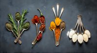 Colorful spices and herbs arranged in vintage spoons on dark stone background, top view flat lay for food and cooking concepts.