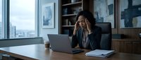 Stressed African American businesswoman experiencing headache while working on laptop in modern office with city view and coffee cup on desk.
