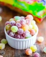 Colorful sugar-coated gummy candies in white ceramic ramekin on wooden surface. Assorted fruit flavored sweets in pink, yellow, and green with powdered coating.