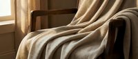 Cozy armchair draped with soft beige throw blanket near sunlit window, creating warm, inviting interior design atmosphere for home decor projects.