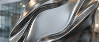 Abstract metallic sculpture with flowing curved forms creating dynamic waves and reflective surfaces in modern architectural setting.