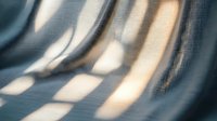 Abstract light and shadow patterns creating soft geometric shapes on textured surface. Natural window blinds casting warm sunlight stripes for modern interior design.