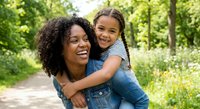 Happy African American mother and daughter embracing outdoors in sunny park, showing love and family bonding during summer day together.
