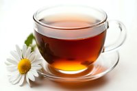 Glass cup of herbal tea with fresh chamomile flower on white background, warm amber liquid glowing in transparent teacup, natural wellness drink.