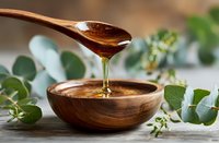 Golden honey dripping from wooden spoon into bowl with fresh eucalyptus leaves, natural organic sweetener for healthy cooking and wellness.