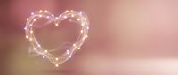 Glowing heart shape made of warm white fairy lights on soft pink gradient background for romantic Valentine's Day celebration and love concepts.