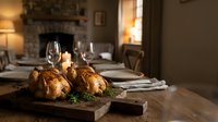 Roasted chicken dinner on wooden board with wine glasses in cozy dining room with fireplace. Perfect for restaurant menus and food advertising campaigns.