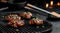Juicy grilled chicken thighs with teriyaki glaze and sesame seeds on black cast iron grill pan, garnished with fresh green onions. Dark moody food photography.