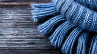 Cozy knitted blue scarf with fringe detail on rustic wooden background. Soft wool texture and warm winter accessory creating seasonal atmosphere.