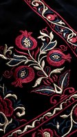 Intricate floral embroidery on black fabric featuring red pomegranates and ornate scrollwork patterns. Traditional needlework craft for textile design projects.