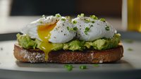 Poached eggs with runny yolk on mashed avocado toast garnished with microgreens and black pepper, served on rustic dark bread against blurred background.