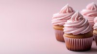 Pink frosted vanilla cupcakes with swirled buttercream topping on soft pink background with copy space, fresh homemade dessert for celebration or party.