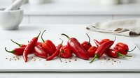 Fresh red chili peppers arranged on white surface with scattered seeds, ideal for food styling, cooking blogs, recipe websites, and culinary publications.