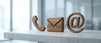 Wooden communication icons including phone, envelope and email symbol arranged on white surface in modern office environment for business contact concepts.