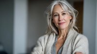 Confident mature woman with silver hair wearing cozy beige cardigan, smiling gently against soft-focus background. Perfect for wellness, aging gracefully, or retirement planning.