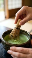 Person whisking matcha powder in ceramic bowl with bamboo whisk, preparing traditional green tea beverage for wellness and culinary use.