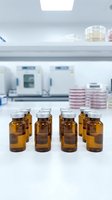 Amber glass vials arranged on laboratory bench with scientific equipment and petri dishes in sterile research facility background for pharmaceutical testing.