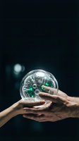 Two hands holding transparent sphere containing green and white capsules against dark background, symbolizing healthcare collaboration, medicine sharing, pharmaceutical partnership.