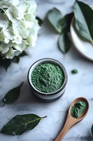 Green matcha tea powder in black ceramic bowl with wooden spoon on marble surface, white hydrangea flowers and fresh green leaves creating zen atmosphere.