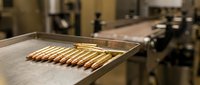 Manufacturing ammunition cartridges on industrial production line with brass casings arranged in factory setting for defense industry applications.