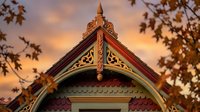 Victorian gingerbread house detail with ornate wooden trim against autumn sunset sky. Architectural heritage home exterior design element.