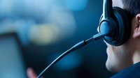 Close-up profile of male customer service representative wearing headset with microphone against blurred blue background, working at call center.