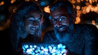 Mature couple illuminated by blue light from digital device, sharing intimate moment against blurred bokeh background at night. Romantic evening mood.
