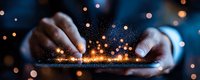 Hands holding digital tablet with magical glowing particles and light effects emerging from screen against dark background with bokeh lights.