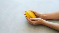 Hands holding fresh yellow mango on white surface, tropical fruit produce for healthy eating, nutrition, and food styling projects.