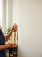 Man with medium skin tone holding empty wine bottle indoors near window with natural light, suitable for alcohol awareness, addiction recovery, sobriety, and lifestyle editorial content.