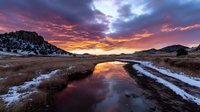 Mountain landscape with dramatic sunset sky reflected in stream during winter season creating stunning natural scenery for outdoor adventure and travel photography.