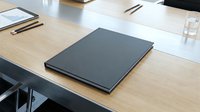 Professional business meeting setup with closed black notebook on wooden conference table surrounded by office supplies and water glass.