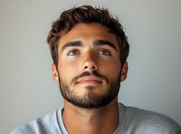 Portrait of young Caucasian man with beard and brown hair looking upward with contemplative expression against neutral background.