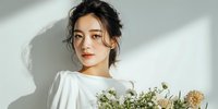 Young Asian woman in white dress holding dried flower bouquet with natural window light and shadows creating elegant portrait for lifestyle photography.