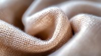 Soft waves of natural beige burlap fabric create gentle folds and curves in macro photography, showing detailed textile weave pattern and texture in neutral tones.