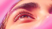 Close up macro shot of eye with long eyelashes and professional makeup in pink neon lighting showing glamorous beauty details and cosmetic artistry.