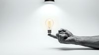 Hand holding glowing vintage Edison bulb under pendant lamp against white wall background symbolizing creativity innovation and bright ideas.