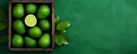 Fresh whole and sliced limes in rustic wooden box on green background with leaves, top view. Citrus fruits for cocktails and cooking.