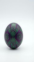 Decorative purple Easter egg with intricate green geometric patterns and traditional folk art motifs isolated on white background for holiday designs.